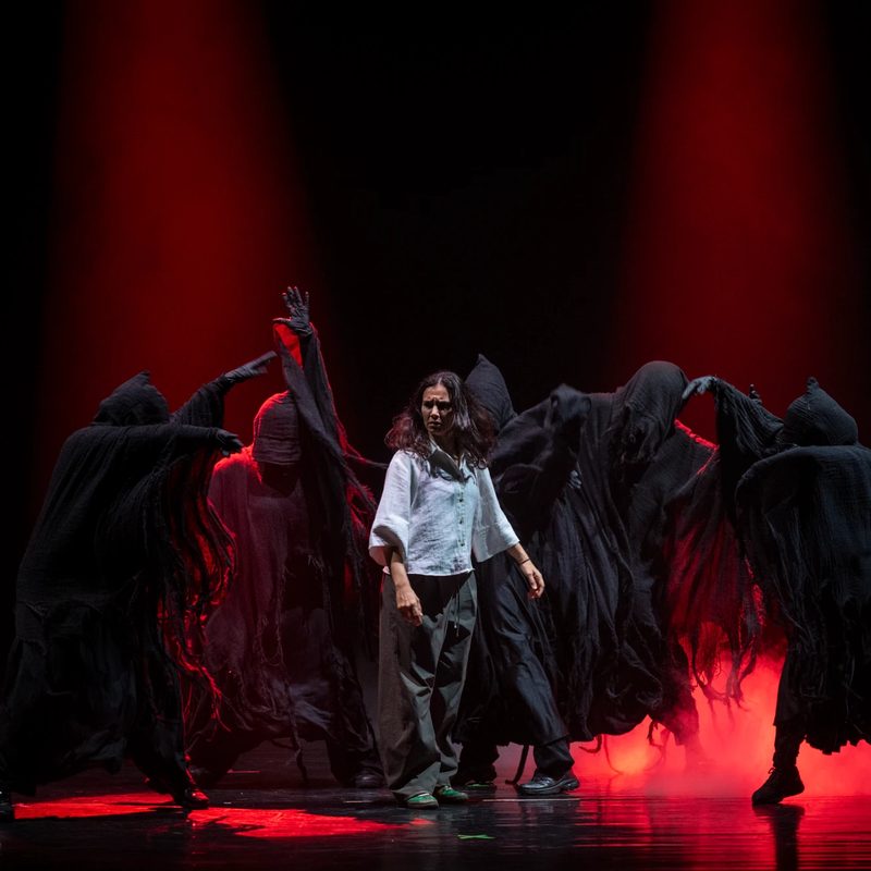 Still Standing 2026 — figuras encapuchadas rodean a la protagonista bajo luz roja
